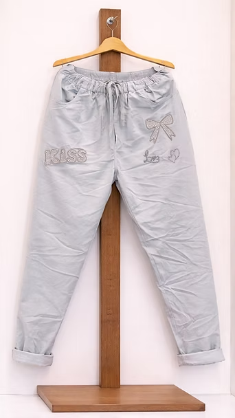 Pantalones de color gris claro colgados en una percha de madera sobre un fondo blanco.