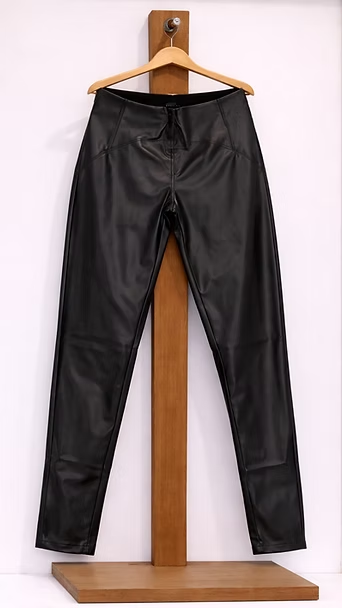 Pantalones de cuero negro colgados en una percha de madera sobre un fondo blanco.