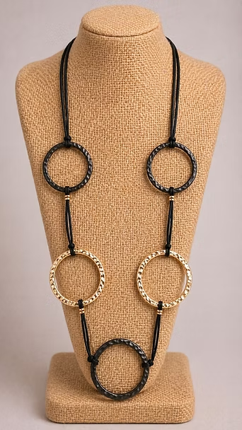 Collar de cuentas negras y doradas exhibido sobre un busto de joyería color canela.