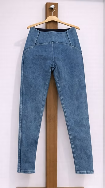 Unos pantalones vaqueros azules colgados en una percha de madera contra una pared clara.