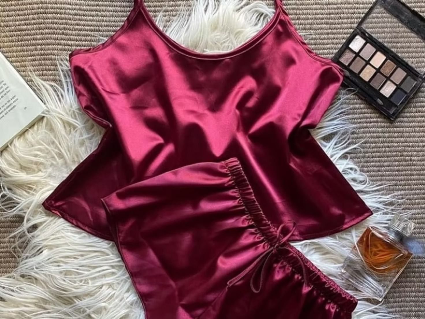 Top de satén magenta y falda fruncida sobre una alfombra de piel blanca con paleta de maquillaje y perfume cerca.