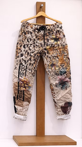 Pantalones cargo con estampado de leopardo y diseño de retazos colgados en un soporte de madera.