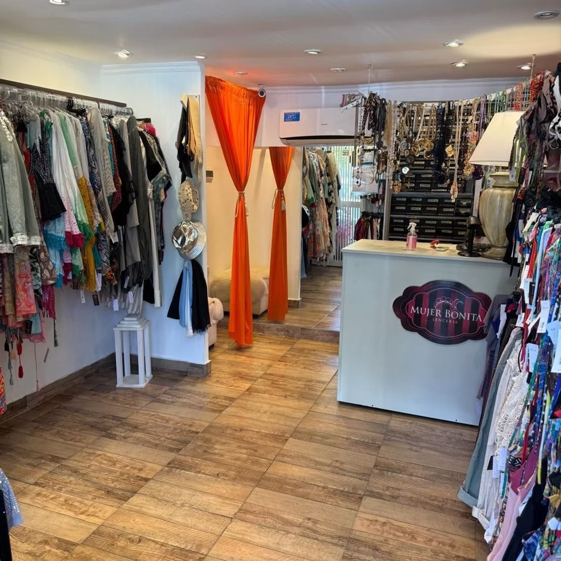 Boutique de ropa con percheros llenos de prendas coloridas, suelo de madera y un mostrador en la parte trasera.