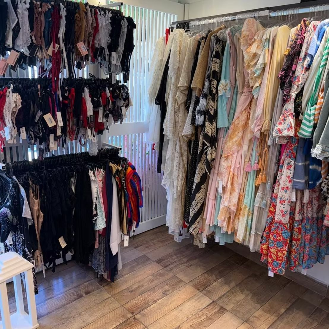 Boutique de ropa con percheros de vestidos, blusas y accesorios en una luminosa habitación de esquina.