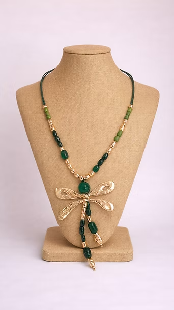 Collar de cuentas verdes y doradas con colgante de mariposa sobre un busto de exhibición beige.