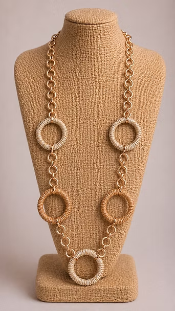 Exhibidor de collar beige con una larga cadena dorada y cinco anillos circulares sobre un busto de arpillera.