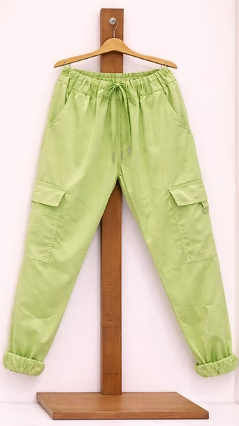 Pantalones cargo de color verde claro colgados en un soporte de madera.