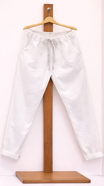 Pantalones blancos colgados en un soporte de madera sobre un fondo claro.