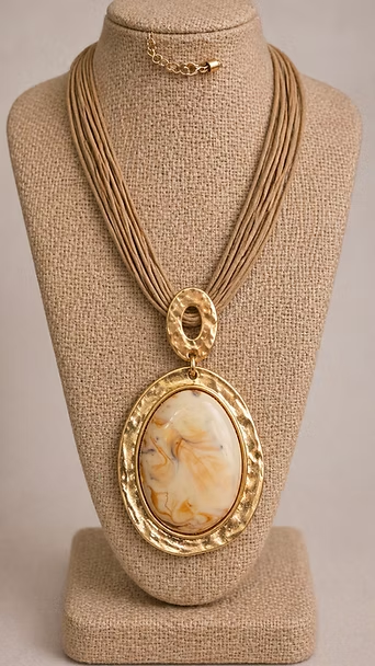 Collar con colgante ovalado de oro con una piedra jaspeada color crema sobre un busto de exhibición beige.
