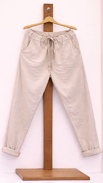 Pantalones de color beige claro colgados de un soporte de madera, con puños enrollados y cintura ajustable con cordón.