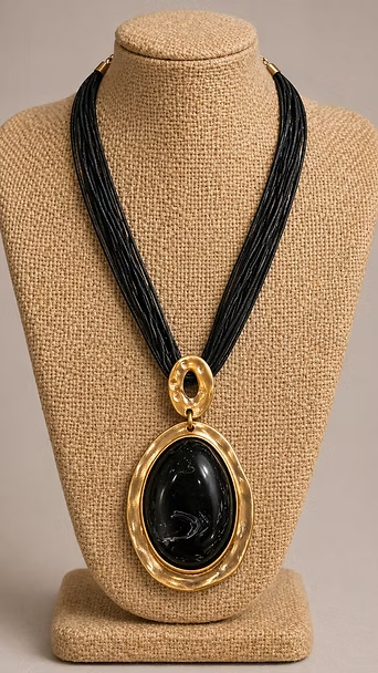 Collar de cuentas negras con un gran colgante ovalado de piedra negra sobre un busto de exhibición color canela.