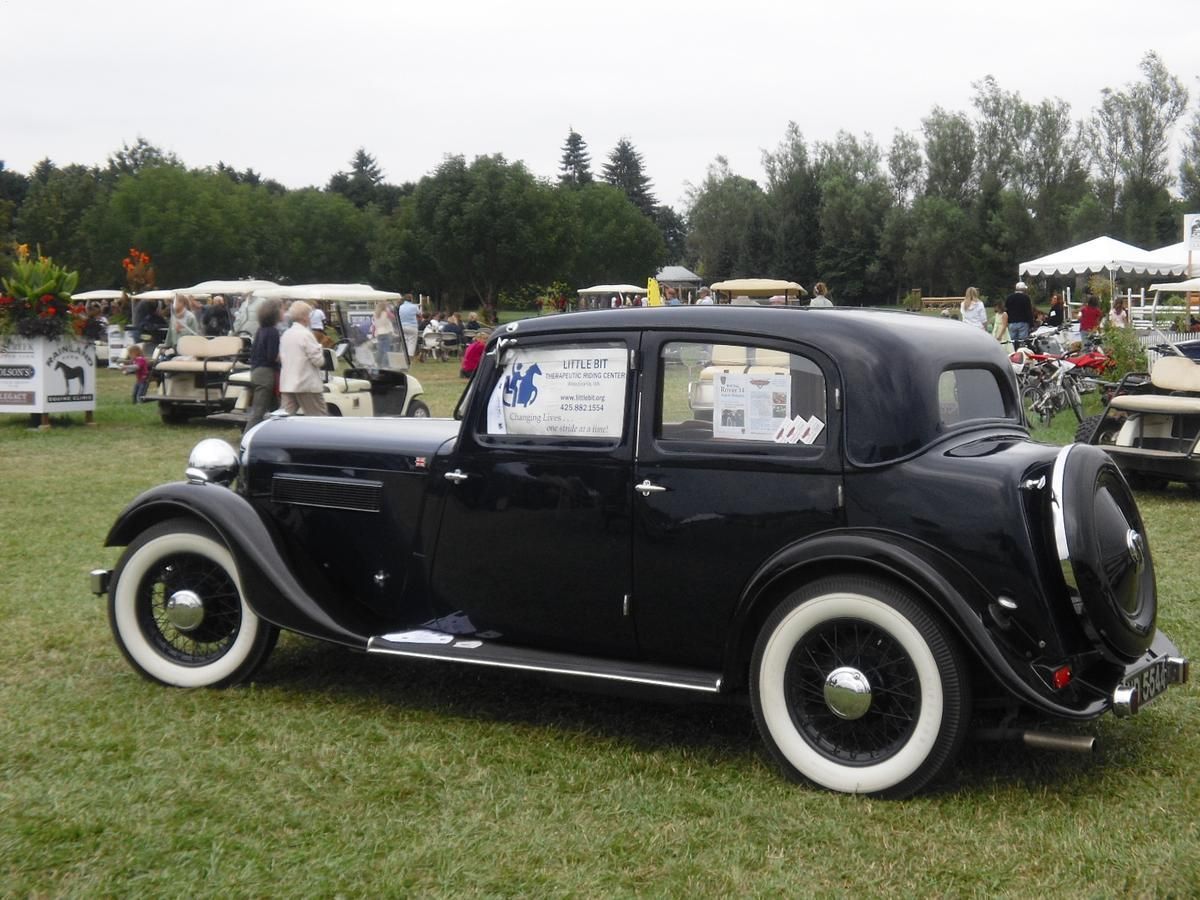A black car with white tires is parked in a grassy field