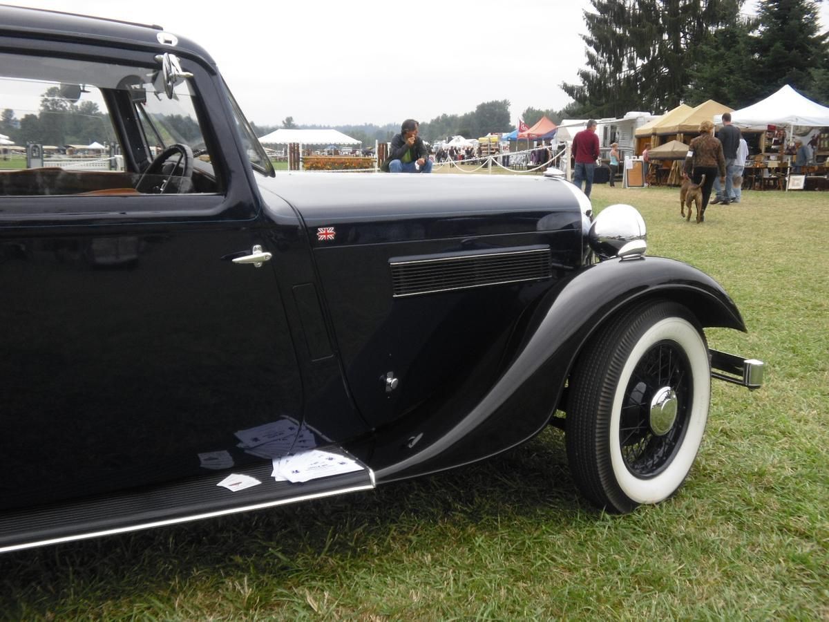 A black car with white tires is parked in a grassy field