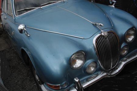 a blue jaguar car is parked on the side of the road .