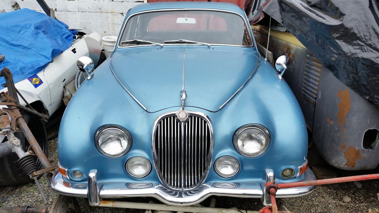 A blue jaguar car is parked in a gravel lot