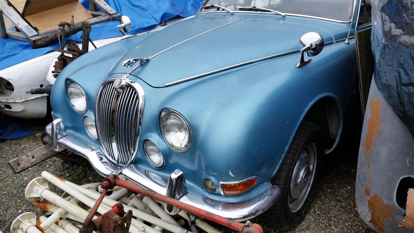 A blue car is parked next to a pile of junk.