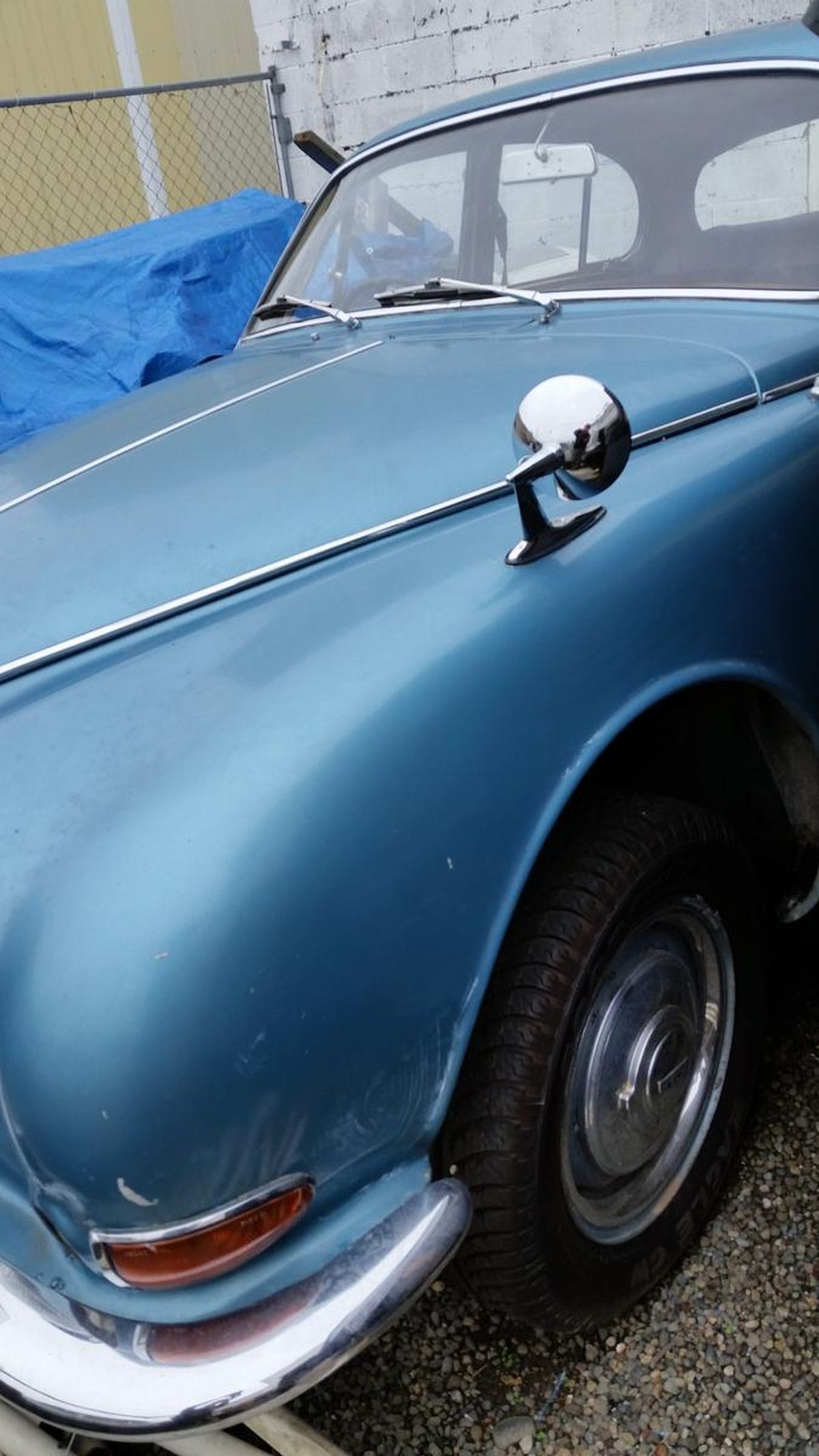 A blue car with a mirror on the hood is parked in a parking lot.
