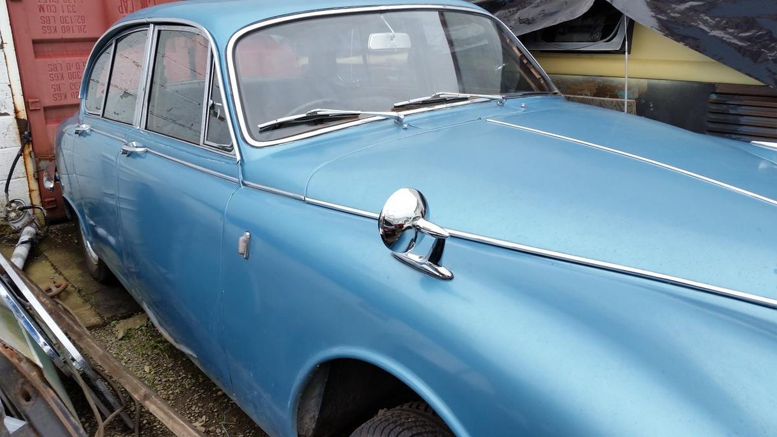 A blue car is parked in front of a red container.