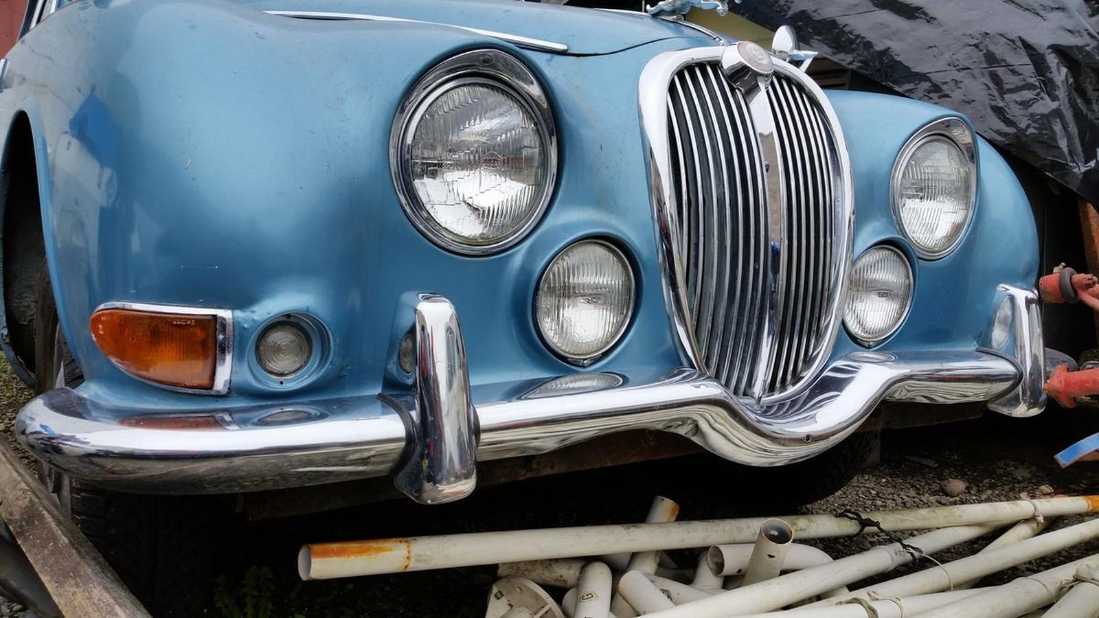 A blue car is sitting on a pile of pipes.
