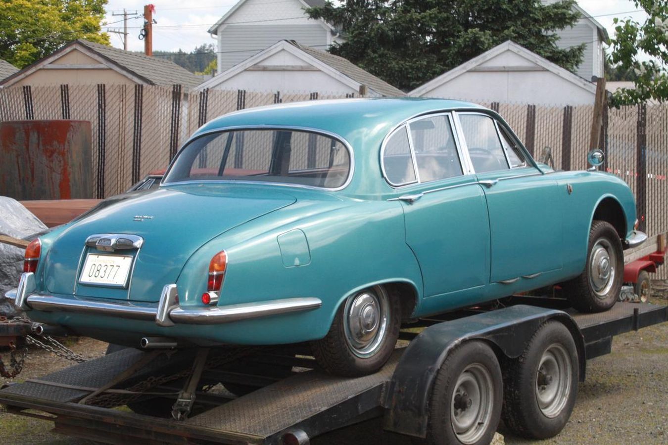 A blue car is sitting on a trailer with a license plate that says lg-127