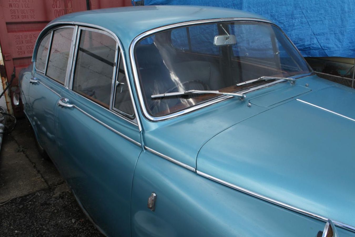 A blue car is parked in front of a blue tarp.