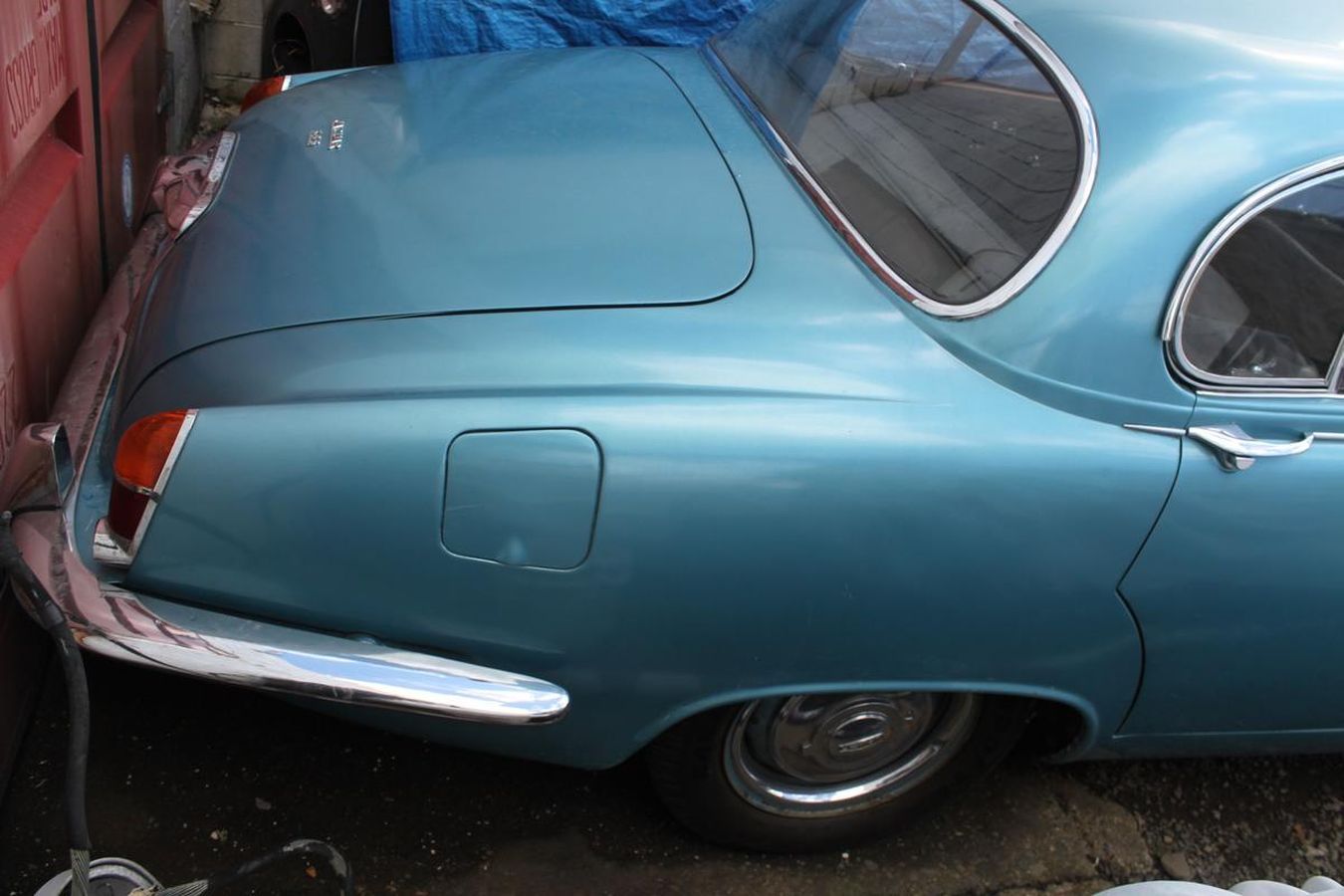 A blue car is parked in front of a red wall