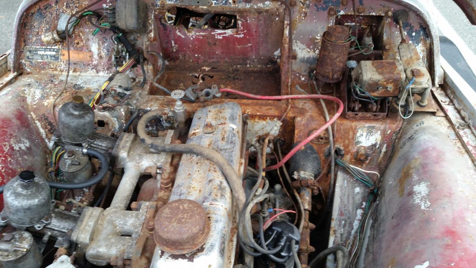 The inside of an old rusty car with a lot of wires coming out of it.