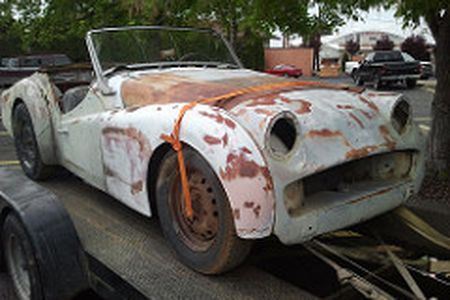 an old rusty sports car is sitting on top of a trailer .