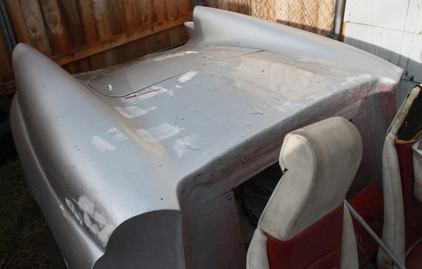 The roof of a car is sitting on the ground next to a wooden fence.