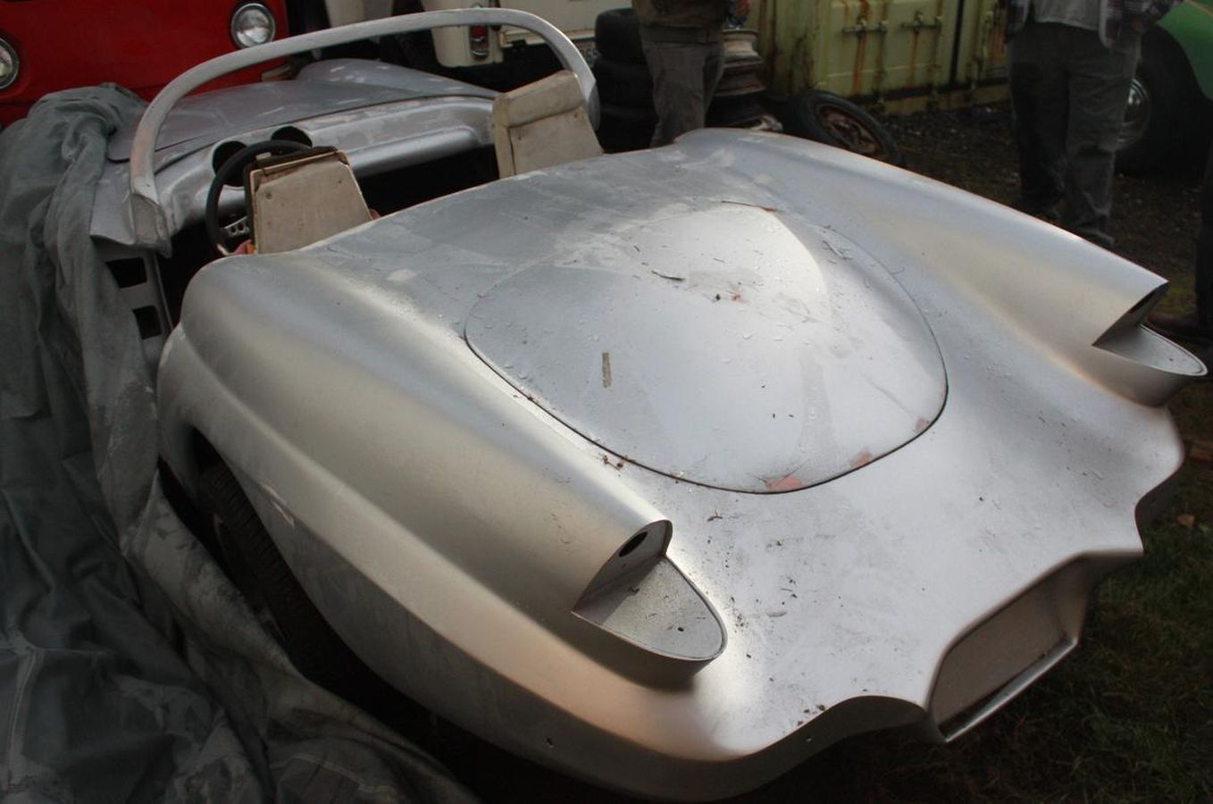 A silver car is sitting on a tarp in the grass