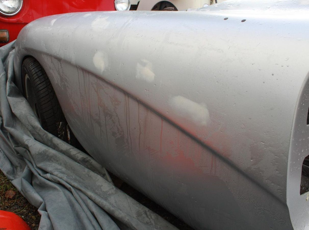 A silver car is covered in a grey cloth
