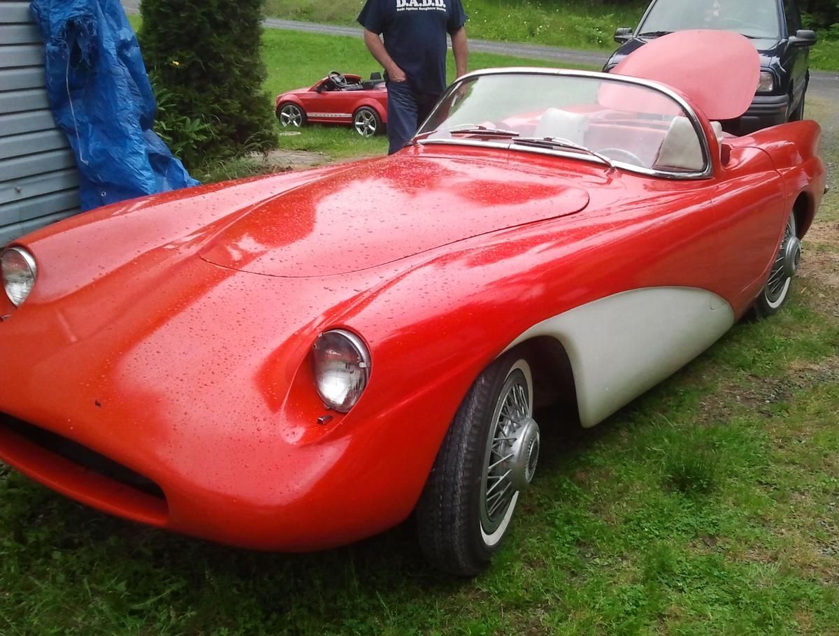A man in a blue shirt stands next to a red sports car