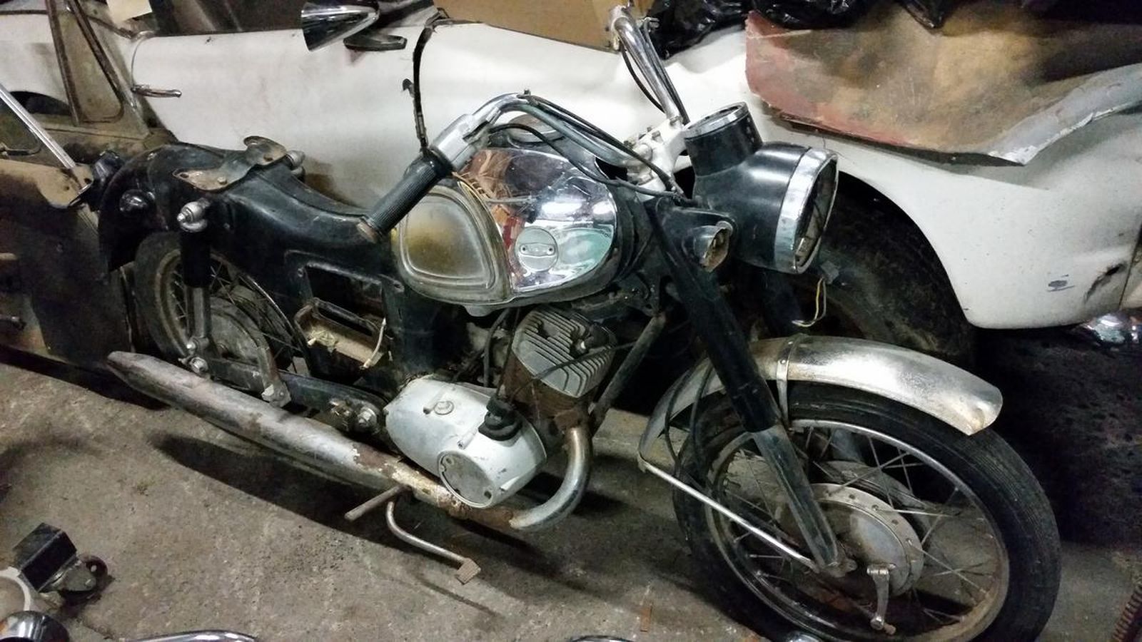 A motorcycle is parked next to a white car in a garage.
