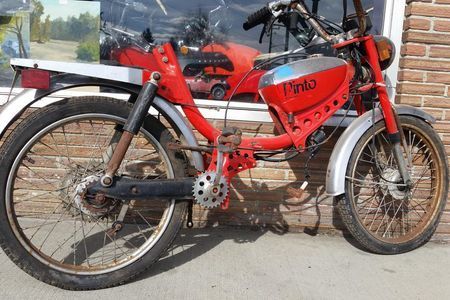 a red pinto motorcycle is parked in front of a brick building
