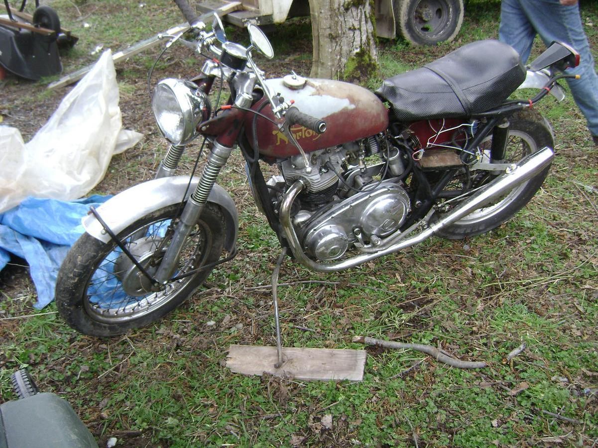 A motorcycle is parked in the grass with a person standing behind it.