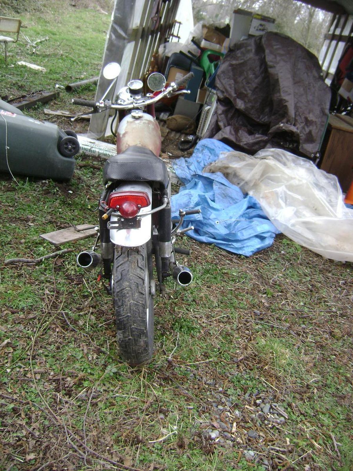 A motorcycle is parked in the grass next to a pile of trash.