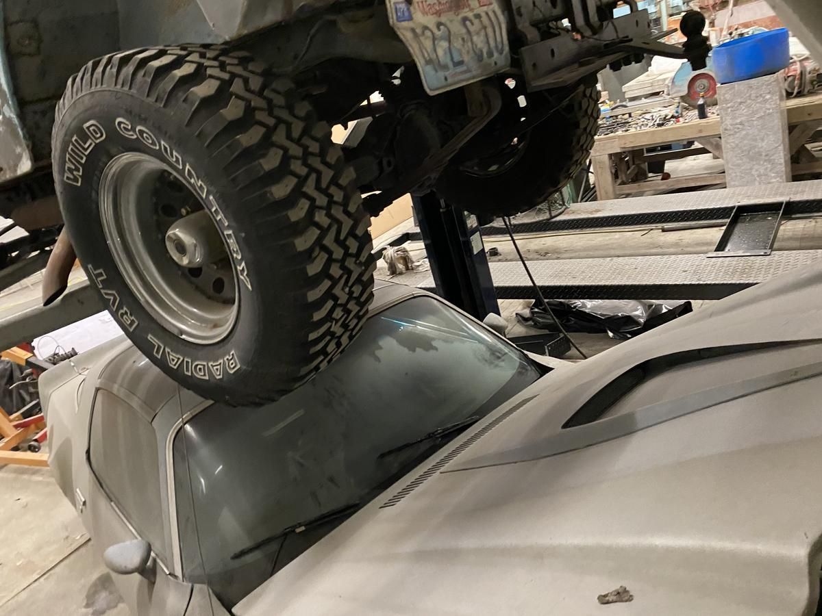 A jeep is sitting on top of a white car in a garage.