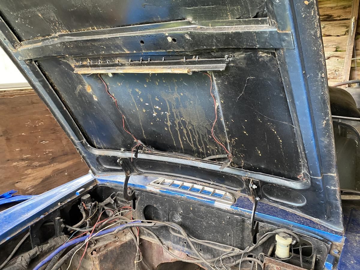 The hood of a blue car is open and dirty.