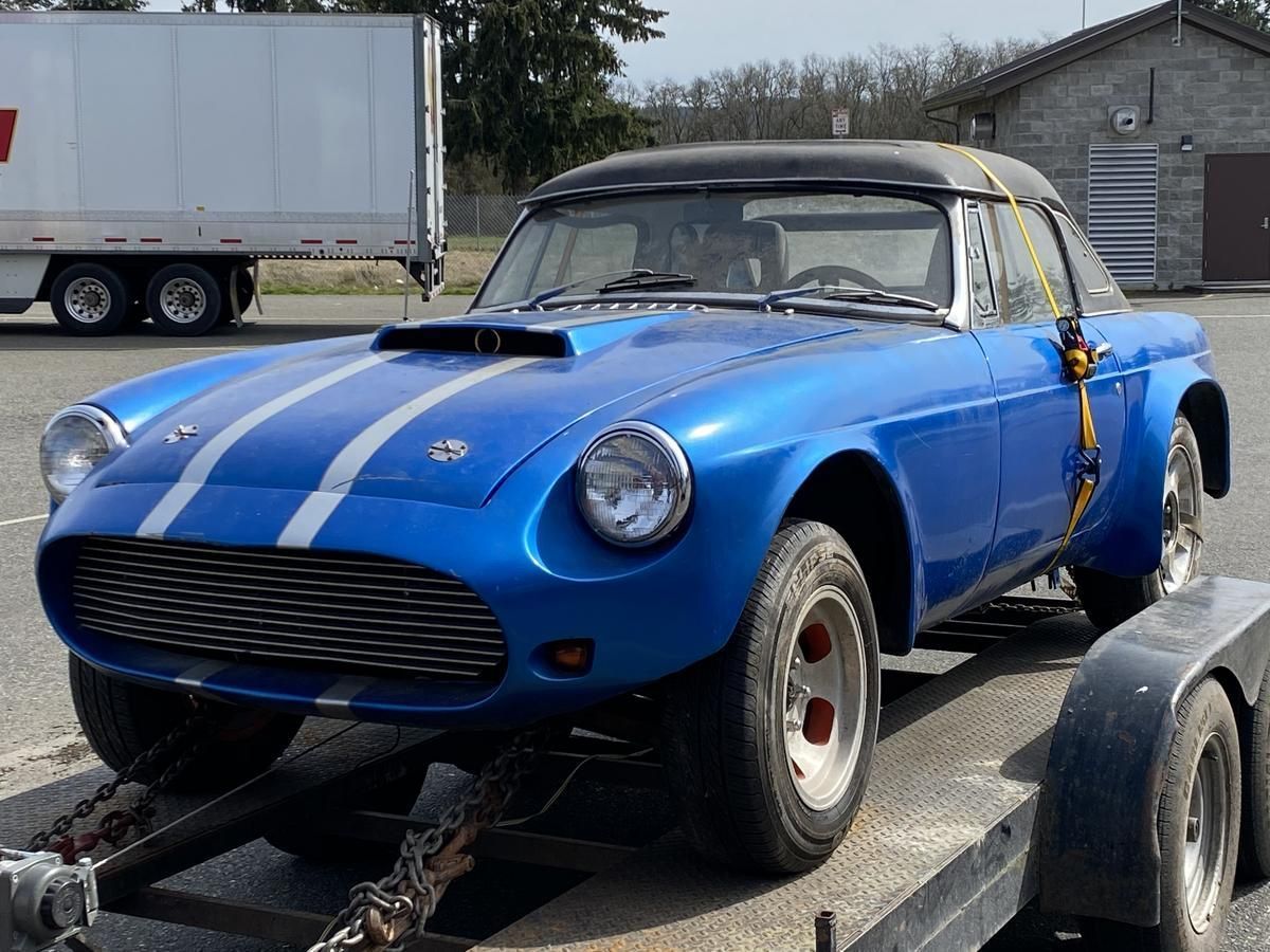 A blue car is on a trailer with a white truck in the background
