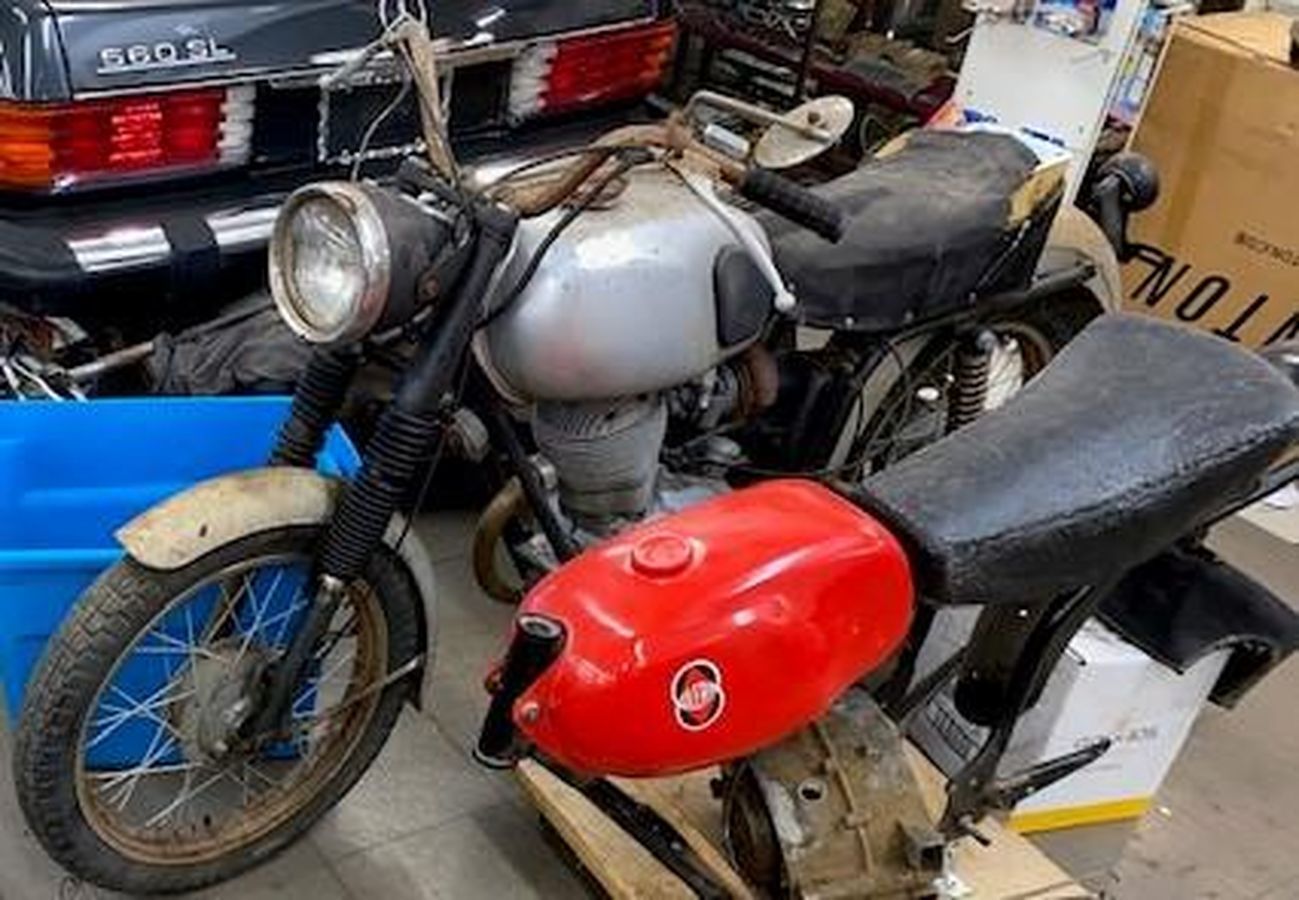 A motorcycle with a red tank is parked in a garage next to a mercedes benz.