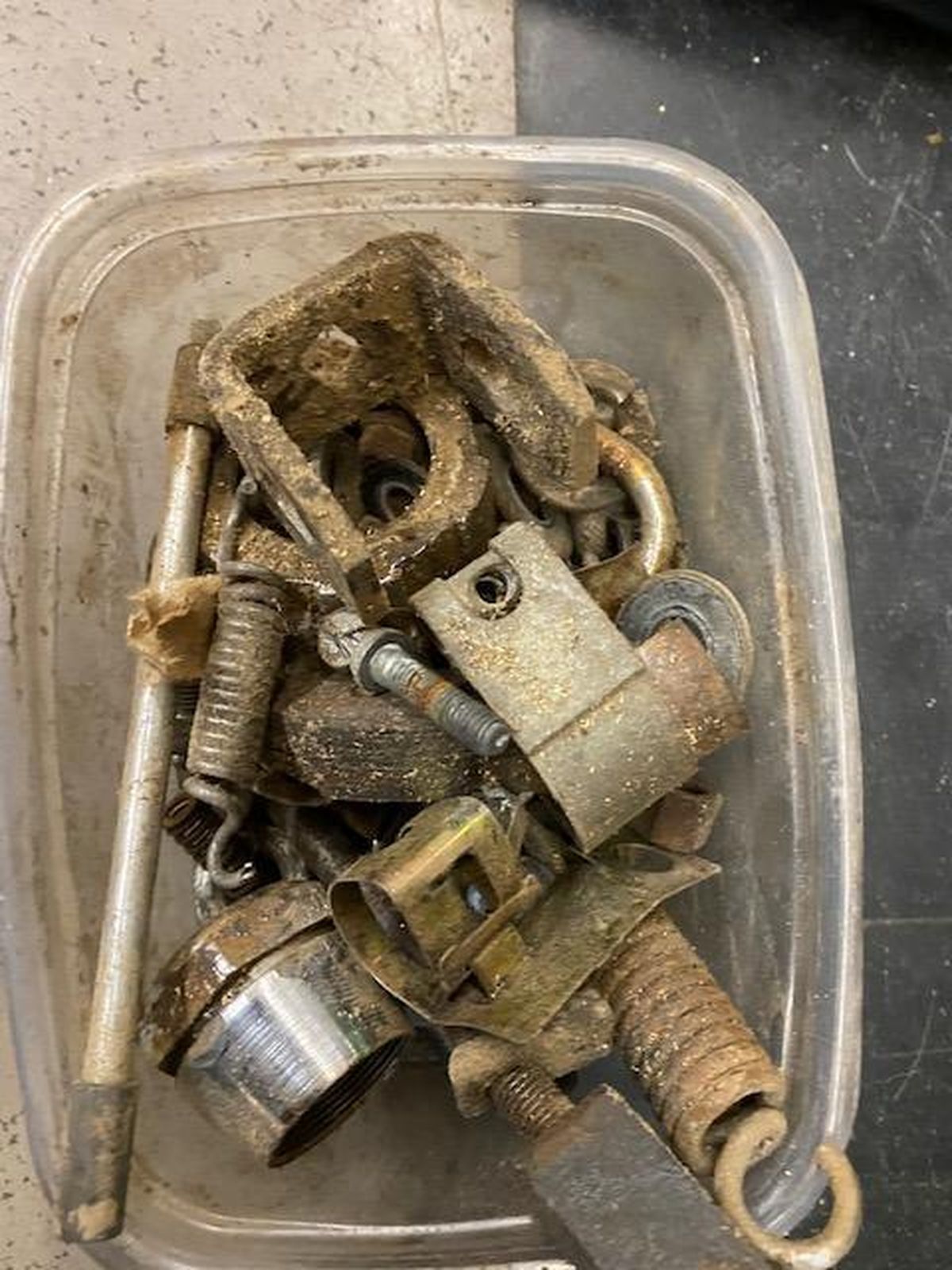 A plastic container filled with rusty metal parts on a table.