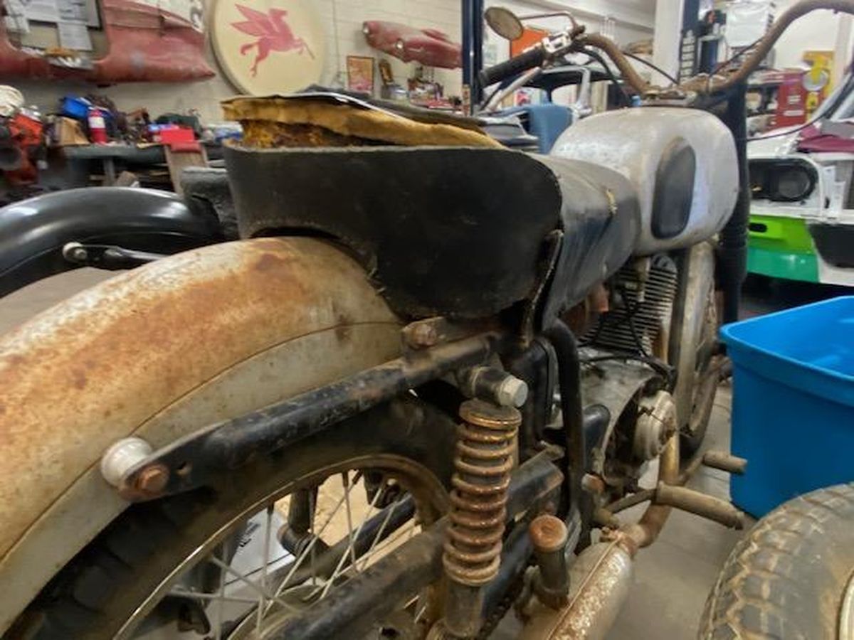 An old rusty motorcycle is parked in a garage