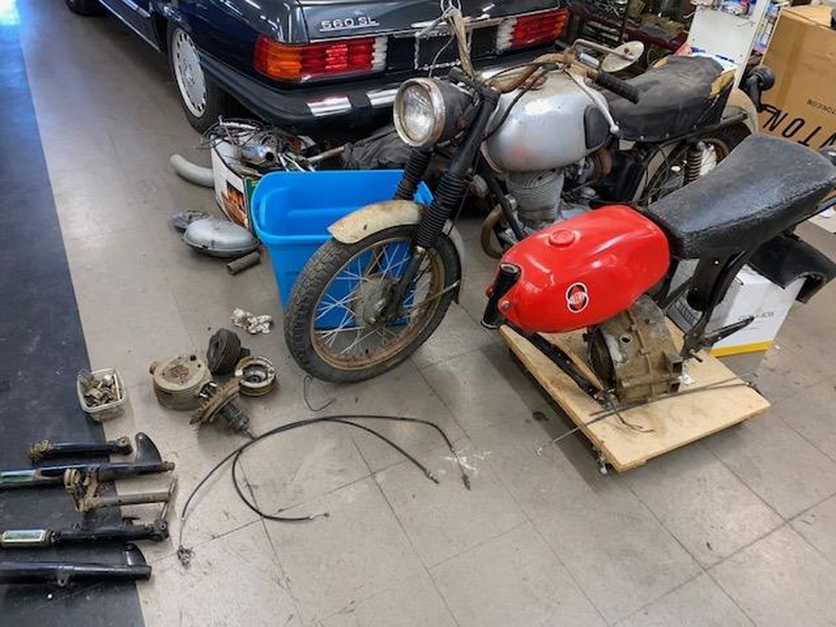 A motorcycle with a red tank is sitting in a garage next to a car.