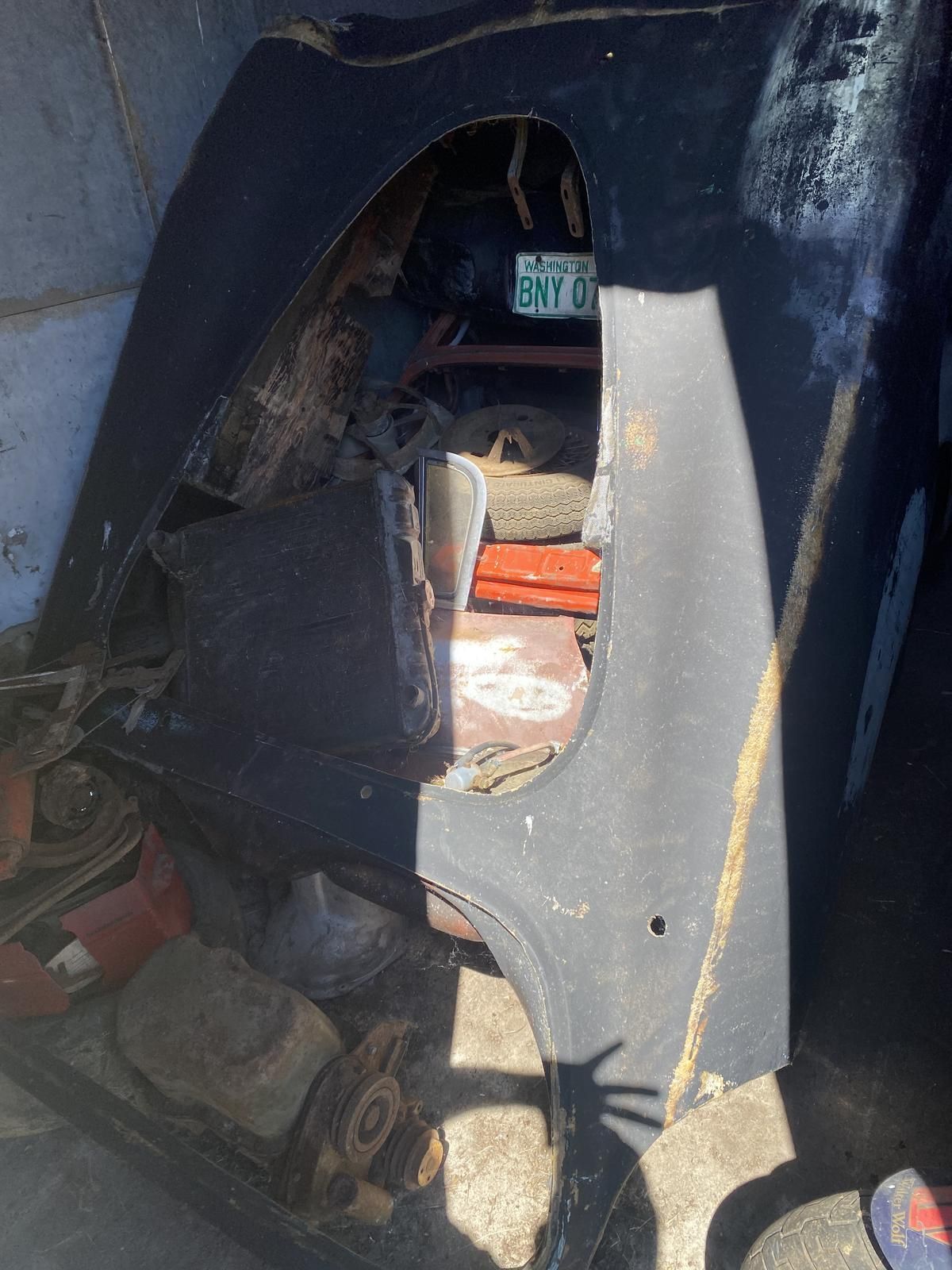 A black car is sitting in a garage with a broken fender.