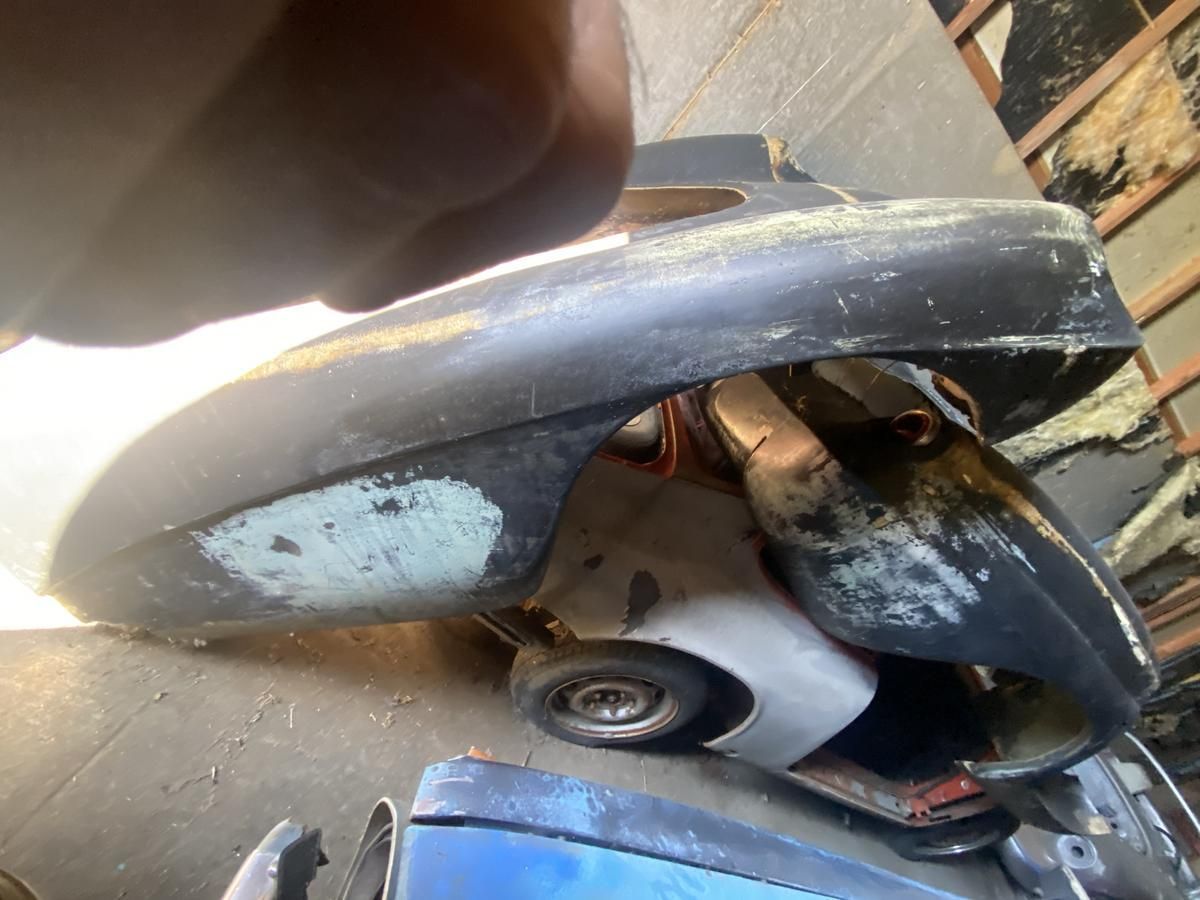 A person is holding a fender of a car in a garage.