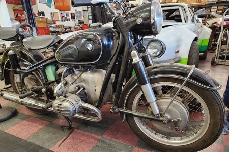 an old motorcycle is parked in a garage next to a car .