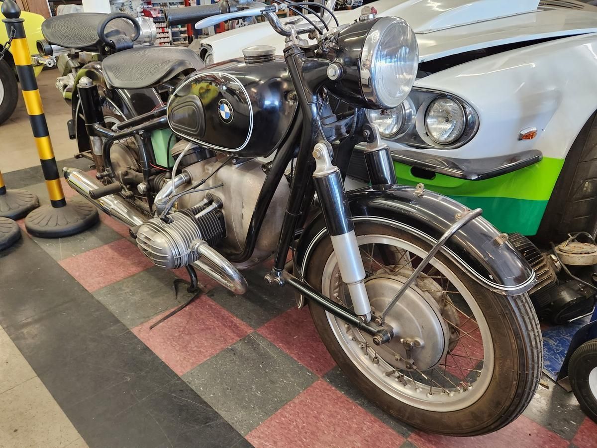 An old motorcycle is parked next to a car in a garage.