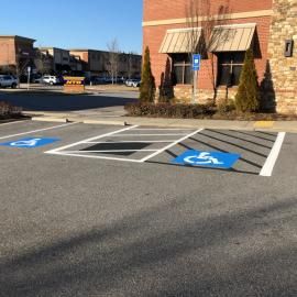 Two accessible parking spots with blue wheelchair symbols and a striped loading zone in a brick building parking lot.