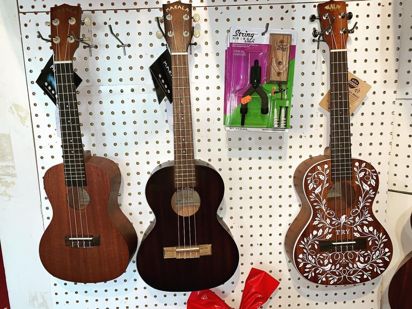 Three brown ukuleles hanging on a pegboard display, with a colorful package in the center.