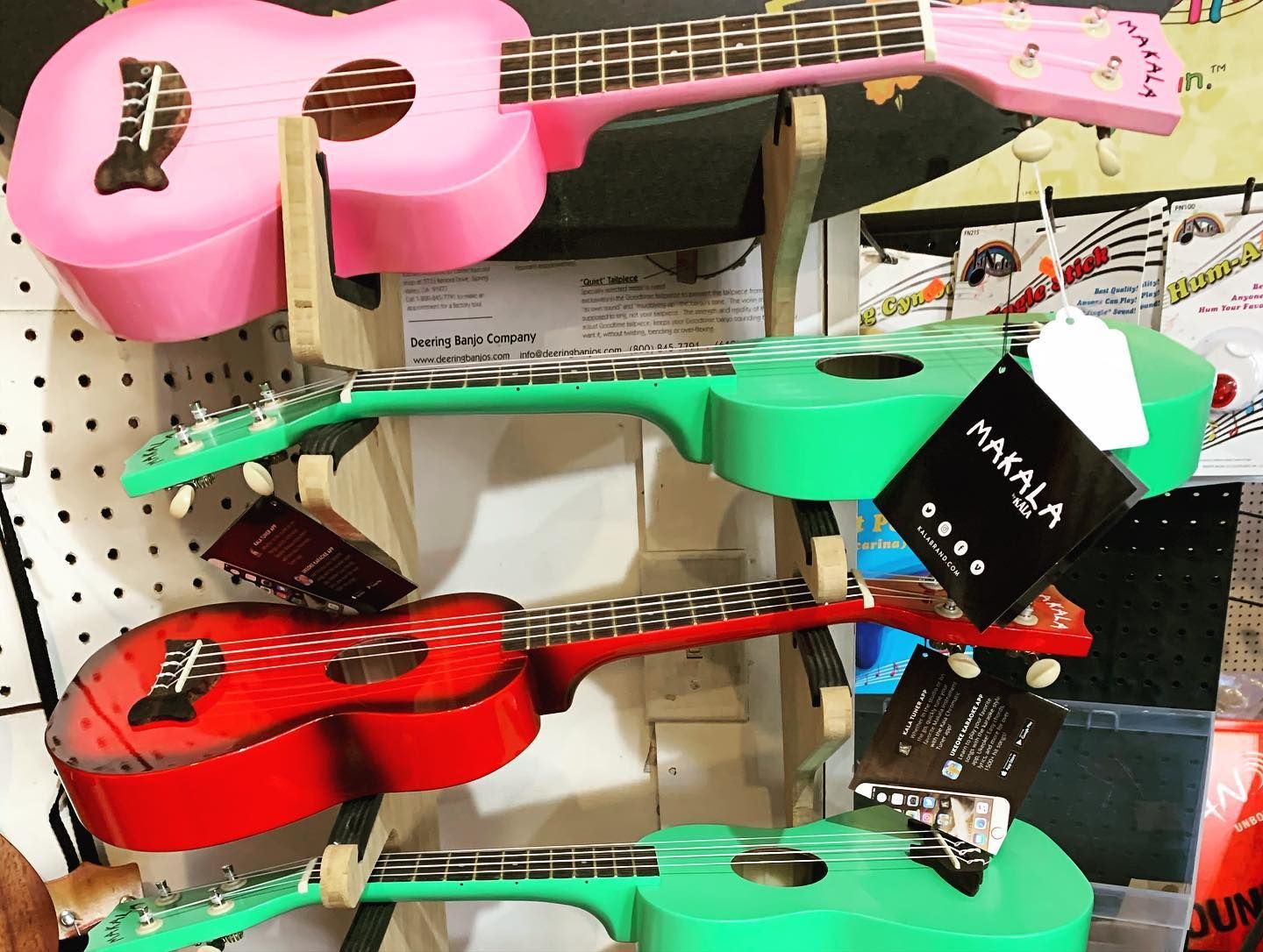Stacked colorful ukuleles in a store display, including pink, green, and red instruments.